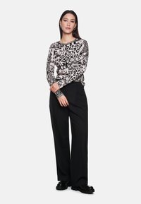 Long-sleeve top with black and white animal print and graphic patterns. Paired with black wide-leg trousers and chunky black shoes.