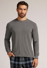 Graues langärmliges T-Shirt aus weichem Material mit Rundhalsausschnitt, kombiniert mit karierter Pyjamahose in Blau- und Schwarztönen.