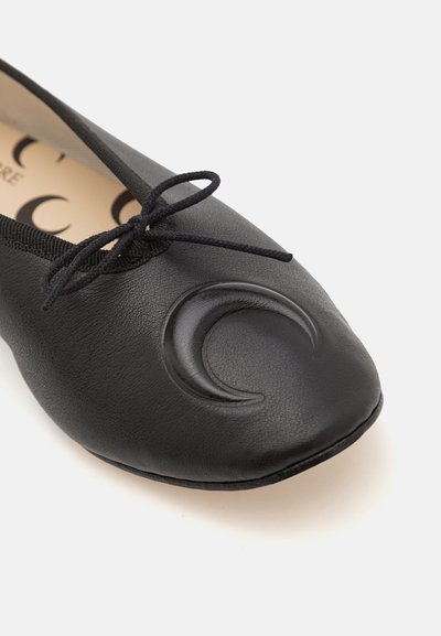 Svart ballerina i texturerat läder, med en dekorativ halvmåne-design på tån och en tunn svart snörning.