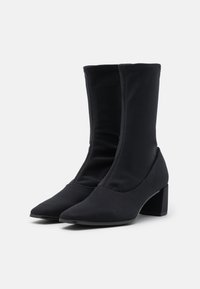 Botas de tobillo de tela negra con una textura suave, puntera puntiaguda y tacón de bloque. El diseño es elegante, con una altura a medio pantorrilla y sin cierres visibles.