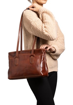 Borsa tote in pelle marrone con due manici lunghi, dettagli cuciti e una texture liscia, tenuta da una persona che indossa un maglione beige.