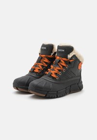 Bottes noires imperméables avec des lacets orange, col en fausse fourrure, semelle en caoutchouc, finition texturée et marque Geox sur la languette et le côté.