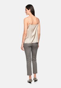 Satin tank top in beige with adjustable straps paired with patterned black and white fitted trousers. Slim-fit design and ankle length.