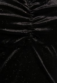 Tecido preto com um design plissado, apresentando partículas douradas cintilantes incorporadas. O material tem uma textura suave e brilhante.