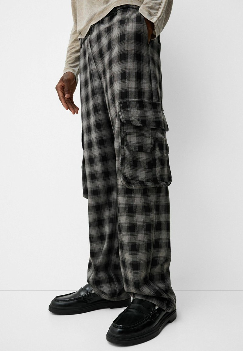 Pantalones cargo de cuadros en negro y gris con bolsillos laterales, hechos de una tela suave; corte de pierna ancha; combinados con mocasines negros.