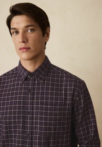 Skjorte med tern i mørk lilla med lyserøde striber. Har krave, brystlomme og sorte knapper. Blød stoftekstur.