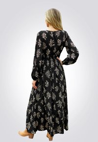 Maxikleid mit langen Ärmeln, schwarzem Stoff mit weißen Blumenmustern, tailliertem Bund, schwingendem Rock und braunen, hochhackigen Stiefeletten.