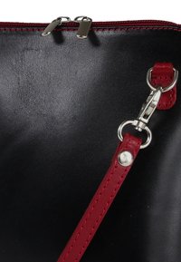 Zwarte leren tas met roodkleurige riemaccenten, ritssluiting en zilverkleurige hardware. Gladde textuur met zichtbare stikseldetails.