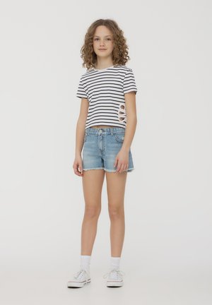 Maglietta a maniche corte a righe con design a taglio abbinata a pantaloni shorts in denim azzurro. Sneakers bianche e calzini alla caviglia completano il look.