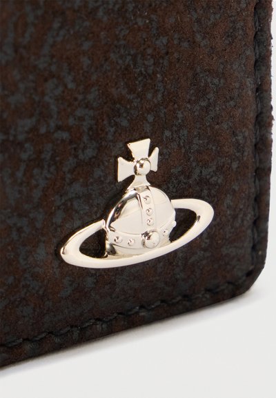 Ασημένια σφαίρα με σταυρό και οριζόντιο δακτύλιο σε κενόγραμμα σε υφή σκούρα καφέ δερματίνης, κοντά στο ραμμένο άκρο.