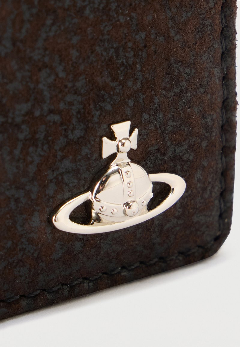 Silberne Kugel mit Kreuz und horizontalem Ringemblem auf strukturiertem dunkelbraunem Leder, nahe der genähten Kante.