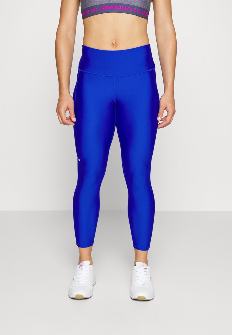 Niebieskie dopasowane legginsy wykonane z gładkiego, elastycznego materiału, z wysokim stanem i subtelnym logo po boku. Noszone z białymi trampkami.