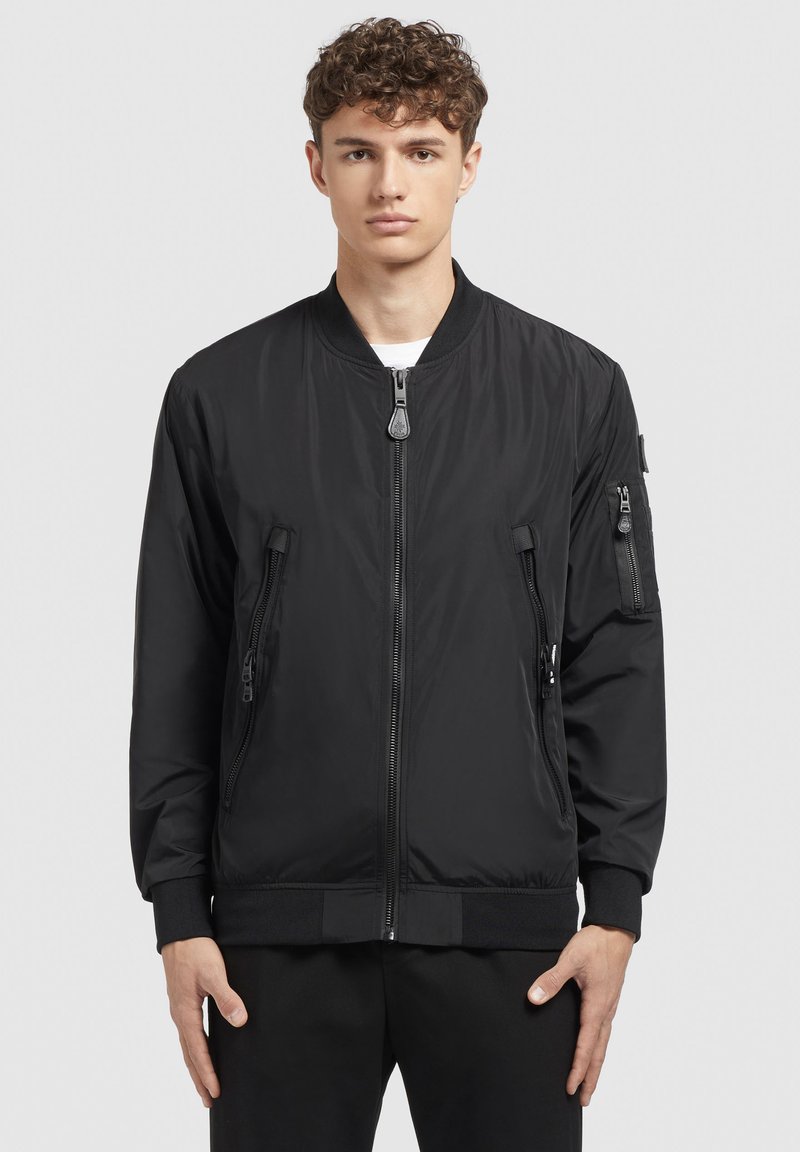 Schwarze Bomberjacke mit einem Reißverschluss vorne, gerippten Bündchen und zwei seitlichen Reißverschlusstaschen. Hergestellt aus glattem, leichtem Stoff mit einem minimalistischen Design.