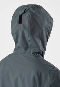 Majica tamno sive nepropusne jakne prikazana sa stražnje strane s crnom tkanom petljom na stražnjem dijelu kapuljače.