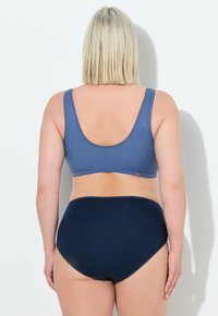 Modrý bezšvový bralet s širokými ramínky a nízkým zadním dílem, spárovaný s vysokými námořnickými kalhotkami. Hladká textura a jednoduchý design.