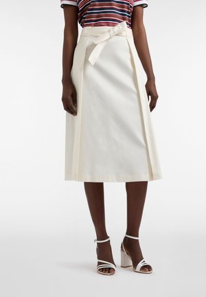 Woman wearing a cream midi skirt with a tied belt, white strappy block-heeled sandals, and a striped short-sleeve shirt.