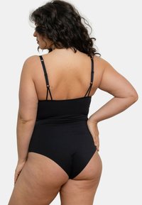 Maillot de bain noir une pièce avec bretelles réglables, texture lisse, ouvertures de jambes hautes et design ajusté. La vue arrière montre une couverture minimale.