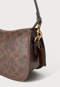 Brown leather handbag with a distinctive circular pattern, gold hardware, and a zip closure. Features a detachable tag and contrast stitching.