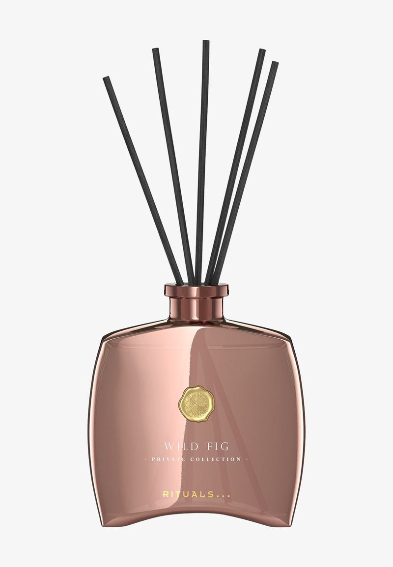 Diffusore con bottiglia di vetro color oro rosa, forma arrotondata, etichetta a rilievo dorata e cinque bastoncini neri per la dispersione della fragranza.