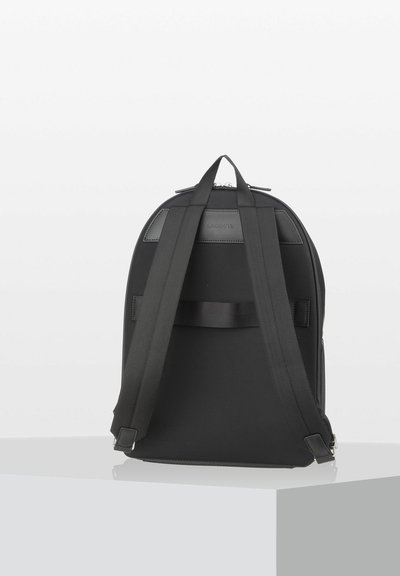 Sac à dos noir en tissu durable avec des bretelles rembourrées, un dessus arrondi et une étiquette logo brillante à l'arrière. Fermeture éclair sur le côté.