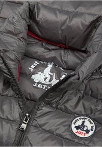 Szara pikowana kurtka puchowa z czerwonym podszyciem, zamkiem z przodu oraz okrągłą naszywką z wizerunkiem skutera i tekstem.