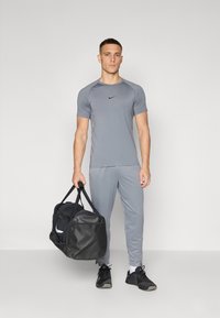 Camiseta deportiva gris con mangas cortas y un logo negro, combinada con joggers grises a juego. Bolsa de deporte negra con acentos blancos.