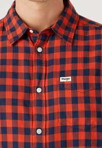 Rood en marineblauw geruit overhemd met een kraag, witte knopen en een klein "Wrangler" label op de borstzak. Gestructureerde stof.