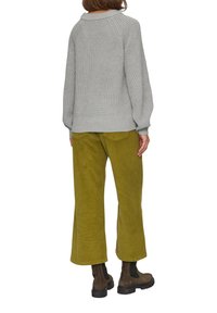 Grijze gebreide trui met een ronde hals, gecombineerd met olijfgroene corduroy wijde broek. Bruine enkellaarsjes zijn ook zichtbaar.
