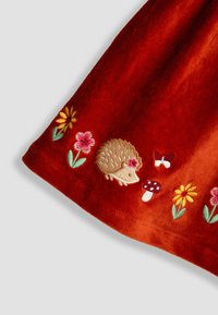 Oranger cordähnlicher Stoff mit besticktem Igel, Pilzen und Blumen. Florale Muster in Rosa, Gelb und grünen Akzenten.