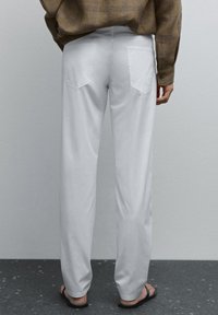 Witte, loszittende broek van katoen, met achterzakken met een gebogen ontwerp. Gedragen met zwarte slippers en een geruite blouse.