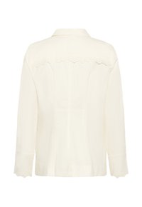 Krēmkrāsas blūze ar garām piedurknēm, kurai manžetēs un aizmugures augšdaļā ir izgriezta mežģīņu apmale, klasisks apkaklis un piegriezums.