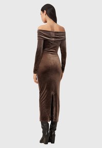 Brązowa, aksamitna sukienka z odkrytymi ramionami i długimi rękawami, dopasowany krój, rozcięcie z tyłu i gładka faktura. Noszona z czarnymi, wysokimi kozakami za kolano.