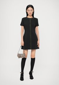 Musta lyhythihainen mekko, jossa keskellä metallisia niittejä, yhdistetty polven korkeisiin mustiin sukkiin ja pieneen harmaaseen käsilaukkuun.