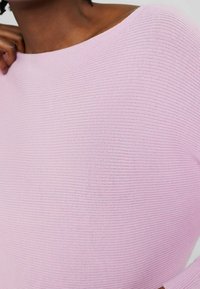 Helles rosa Oberteil aus strukturiertem Rippmaterial, mit lockerer Passform und weitem Ausschnitt. Der Stoff zeigt feine horizontale Linien.