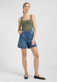 Top verde a costine con scollatura quadrata, abbinato a pantaloni corti in denim blu a vita alta, dotati di tasche laterali e una vestibilità comoda. Ballerine nere.