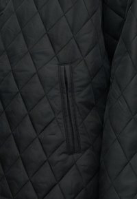 Μαύρο υφασμα με καπιτονέ ραφή σε σχέδιο διαμαντιού και κάθε τσέπη με σχισμή, που δείχνει λεπτομερή υφή και μοτίβο.