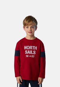 Rotes Langarm-T-Shirt mit dem Aufdruck "NORTH SAILS 1957" in Weiß, marineblauem Akzent an den Ärmeln, aus Baumwollstoff, lockere Passform.