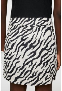 Kort svart kjol med vit bakgrund som har ett djärvt svart zebrastripesmönster, tillverkad av ett slätt, lätt tyg.