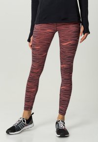 Svart långärmad topp som matchas med färgglada leggings med ett vågigt rött och rosa mönster, tillverkade av stretchigt, texturerat tyg.