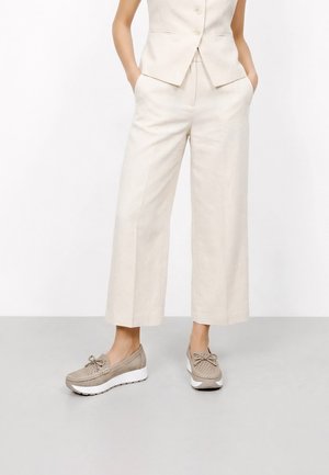 Mujer vistiendo pantalones beige cortos de pierna ancha, chaleco sin mangas a juego y zapatos plataforma sin cordones color topo con diseño perforado y detalle de lazo.