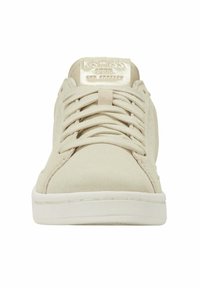 Baskets beiges avec une tige texturée et des lacets plats. Présente un col rembourré et un patch logo brillant sur la languette. Semelle en caoutchouc blanc.