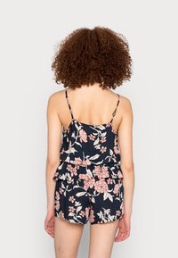 Conjunto de top peplum floral e calções em azul marinho com flores rosas e creme. Alças finas e design em camadas acentuam o tecido leve.