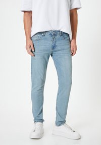 Jeans de denim azul claro con un ajuste Slim. Las características incluyen un diseño clásico de cinco bolsillos, cierre frontal con botón y un ligero desvanecimiento.