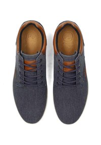 Zapatillas de tela gris con detalles en cuero marrón. Presentan una punta redondeada, un diseño de cinco ojales para atar y una suela de goma texturizada.