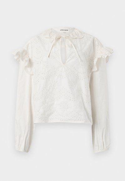 Blouse blanche à manches longues avec broderie œillets, épaules à volants, encolure fendue avec lien, et poignets élastiques.