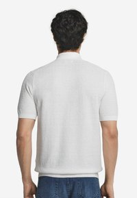 Vit kortärmad polo med texturerad tyg, ribbad krage och manschetter. Finns i en avslappnad passform.