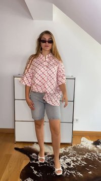 Lühikeste varrukatega roosa mustriga särk punaste detailidega, millele on kombineeritud heledad denimsärgiga lühikesed püksid ja valged sandaalid, asetatuna lehmanaha vaibale.