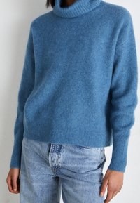 Pull à col roulé bleu clair et confortable, en texture tricotée douce. Associé à un jean en denim clair, avec une coupe ample et un design classique à cinq poches.