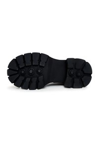 Semelle de botte en caoutchouc noir avec des crampons profonds et des motifs circulaires antidérapants, vue de dessous sur fond blanc.