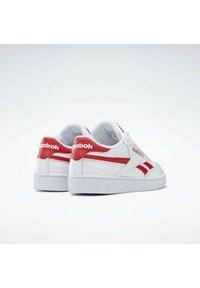 Fehér sneaker piros részletekkel, textúrált bőr felsőrésszel, párnázott cipőpánttal és gumitalppal. A márkaneve a saroknál található.